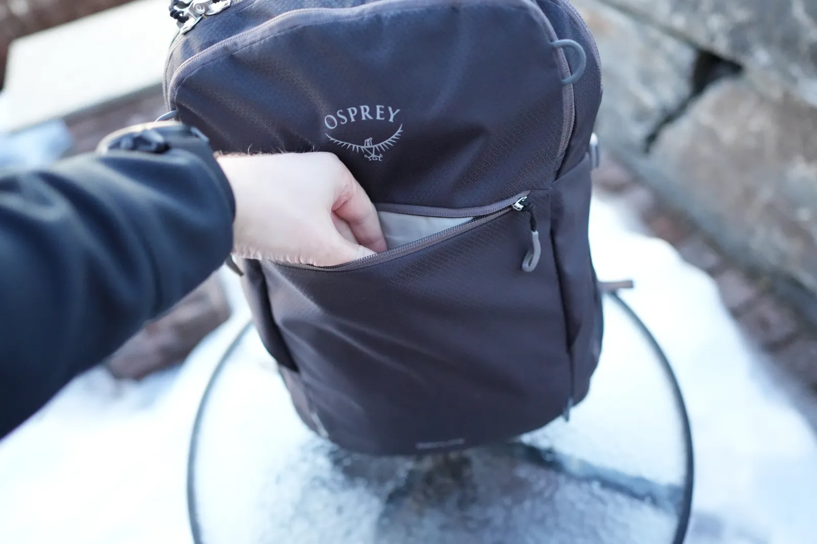 Hand reaching into the Osprey Daylite 35 front zippered pocket, showing easy access with Osprey logo visible above